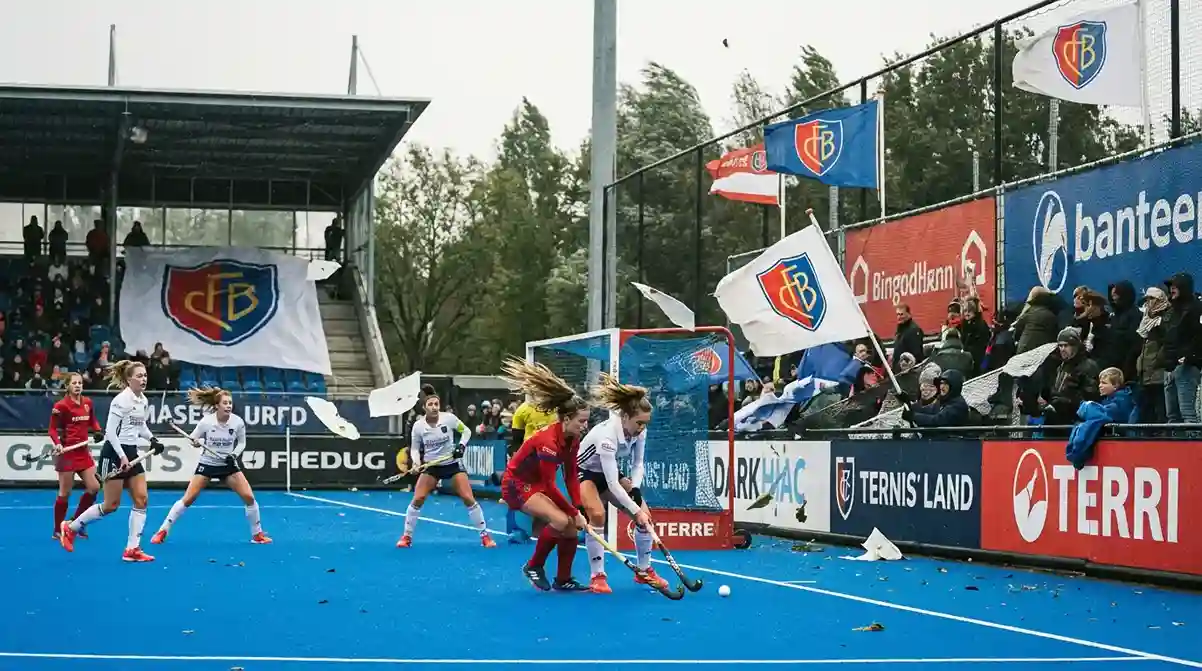 Hockeyspelers in actie op een winderig veld met wapperende vlaggen