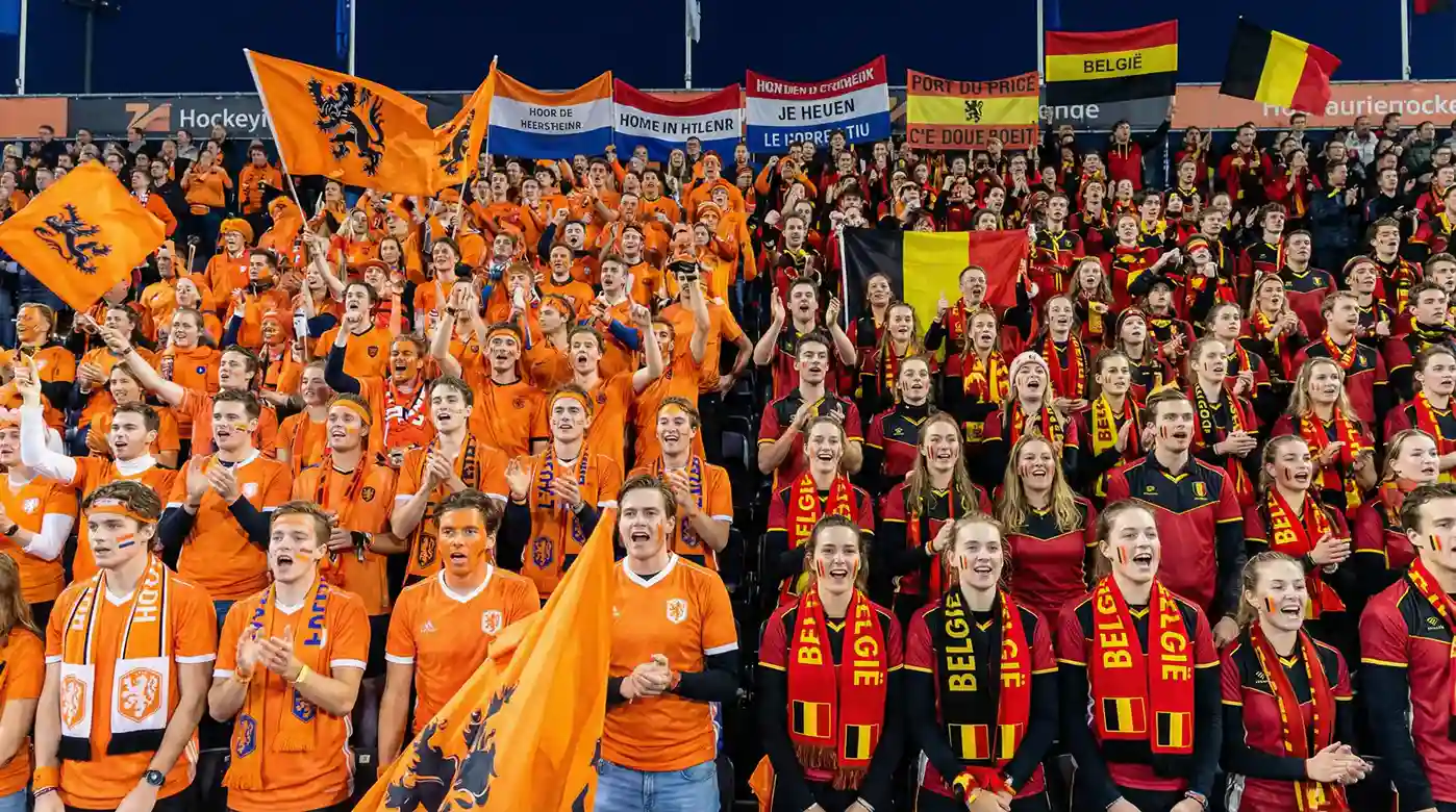 Enthousiaste hockeyfans in oranje en rood die hun teams aanmoedigen